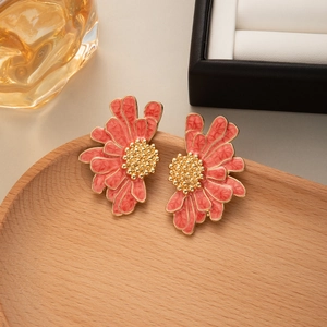 Detailed view of handmade coral pink daisy earrings with golden texture on wood tray