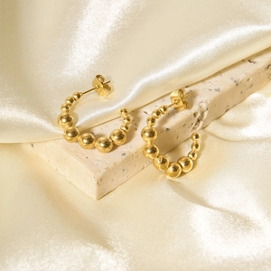 Macro view of gold beaded C-shaped earrings on textured stone and silk fabric