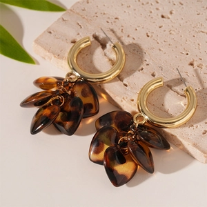 Detail of amber leopard print resin heart earrings on beige stone base with green leaves