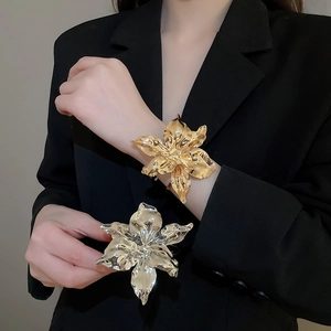 Detail of a large metallic flower cuff bracelet in gold and silver on a black suit sleeve