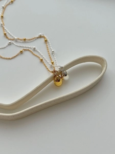 Close-up of gold and silver S925 necklaces with polished water drop pendants on a stand