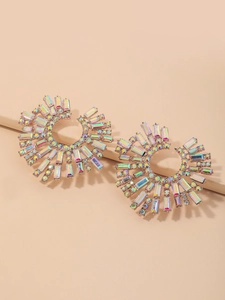 Macro shot of oversized sunburst earrings with shimmering AB crystals on a beige pedestal
