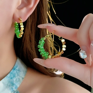 Détail de créoles plaquées or avec cristaux verts et perles dorées portées par un mannequin