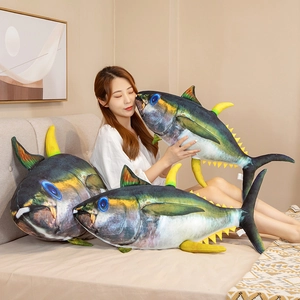Three realistic tuna plush pillows in various sizes held by a person in a cozy bedroom