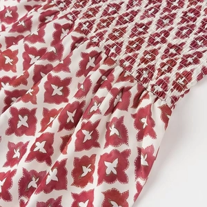 Détail du tissu floral blanc avec motif géométrique rouge et couture smockée élastique