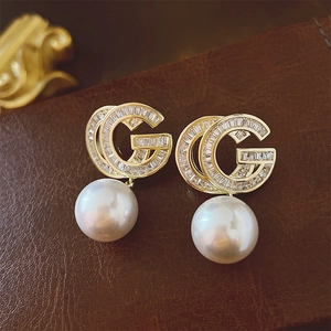 Macro shot of gold double G heart earrings with white pearls and zircons on leather