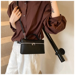 Detailed view of black litchi textured leather handbag worn as a shoulder bag