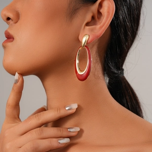 Detail of elegant gold earrings with red drip oil oval inlay worn by a model