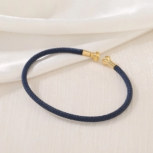 Macro detail of the dark blue woven cord bracelet featuring polished gold metal end caps