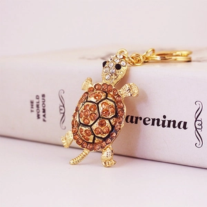 Golden turtle keychain with orange rhinestones on a book background close-up