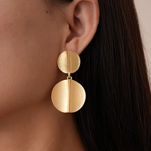 Close-up of golden geometric round earrings with brushed metal texture worn by a model
