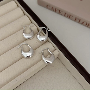 Detailed shot of polished S925 sterling silver U-shaped hoop earrings on beige velvet