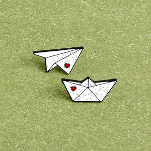 Minimalist paper airplane and paper boat enamel pins with red heart on green background