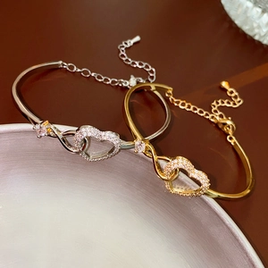 Macro detail of gold and silver bracelets featuring interlocking hearts and pink zircon