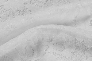 Close-up of white floral lace fabric with intricate cutout patterns and fine texture