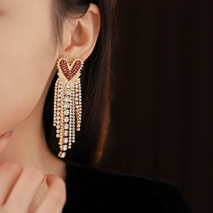 Close-up of red rhinestone heart earrings with long gold tassels on model's ear