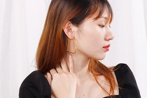 Close-up of golden hollow heart hoop earrings worn by a model against a white fabric background