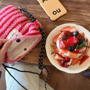 Detail of pink striped plush crossbody bag with snap button closure on wooden table