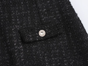 Detailansicht von schwarzem Tweed mit Metallfäden und einem verzierten Strassknopf am Kleid