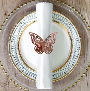 Detail of rose gold butterfly napkin ring with hollow carved design on white ceramic plate