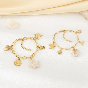 Bracelets dorés thème océan avec breloques coquillage et étoile de mer sur fond de sable blanc