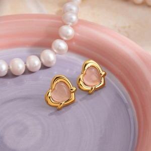 Detail of pink cat eye heart earrings in gold frame on a ceramic plate with pearls
