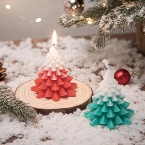 Set of two gradient red and green Christmas tree scented candles in festive snow scenery