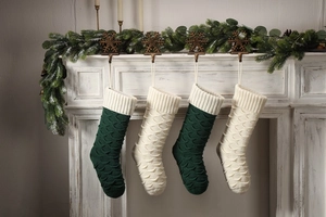 Detail of knit Christmas stockings in dark green and ivory on a rustic white fireplace