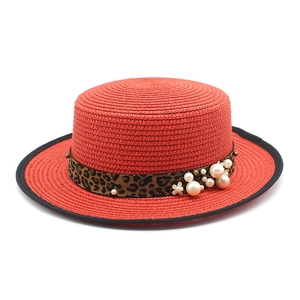 Detailed close-up of a red boater straw hat with leopard ribbon, pearls and floral accents