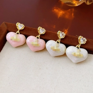 Close-up of pink and white heart earrings with gold plating and sparkling zircon accents