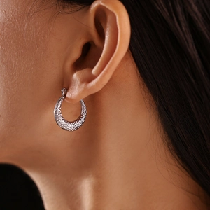 French style C-shaped silver earrings with hammered texture shown on ear lobe