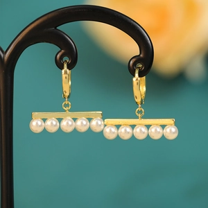 Detailed macro of gold drop earrings with five aligned pearls and hoop closure