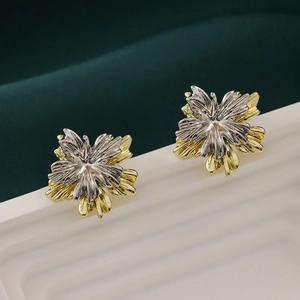 Detail of two-tone metal flower earrings with leaf texture on a green velvet backdrop