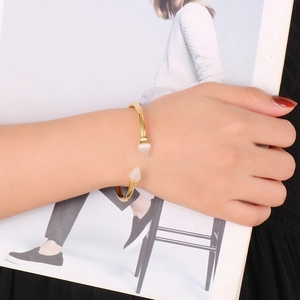 Detail shot of a gold-plated stainless steel cuff bracelet with white conical studs on wrist