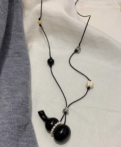 Macro detail of vintage black gourd pendant with mixed beads and woven wax cord necklace