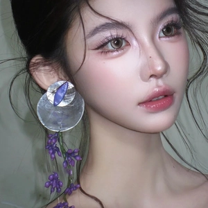Detailed view of large asymmetric shell flower earrings with purple fringe on a model