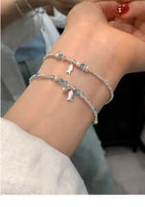 Detail of silver beaded bracelet with freshwater pearls, blue beads and fish charm on wrist