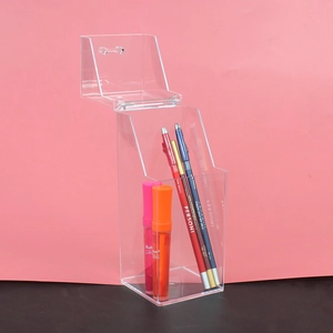 Clear acrylic wall-mounted lipstick and brush holder with lid on a pink backdrop