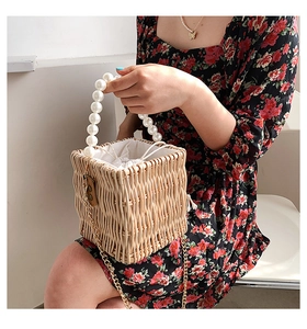 Detail of woven straw basket bag featuring white pearl handle and gold chain strap