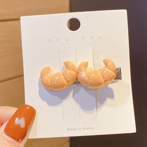 Close-up of cute croissant-shaped hair clip on a white tag being held by hand