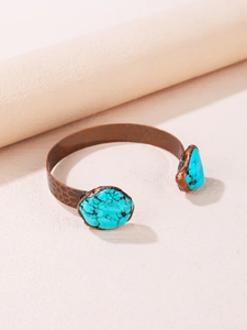 Detailed shot of hammered copper cuff featuring vintage turquoise stones and an open design