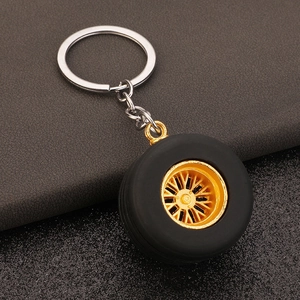 Miniature car tire keychain with black rubber and gold rim on leather surface
