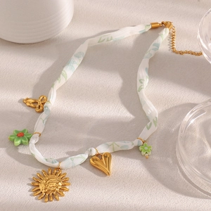 Collier en ruban blanc avec pendentifs soleil, cœur en or et fleurs vertes en vue à plat