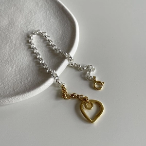 Detailed shot of two-tone heart pendant bracelet with a hollow metal charm on ceramic