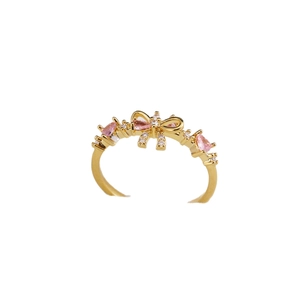 Bague nœud papillon dorée avec zircons roses et blancs étincelants sur fond blanc