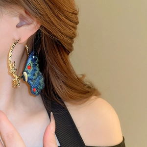 Macro detail of large gold hoop earring featuring an embroidered blue butterfly on model