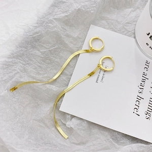 Close-up of golden tassel snake chain earrings on minimalist textured background
