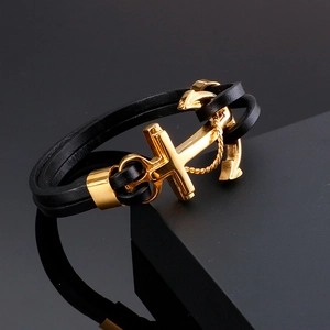 Macro detail of men's black leather wrap bracelet with gold anchor cross buckle on stand