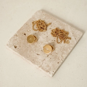 Detail of personalized gold oval initial necklace and rings on beige textured stone