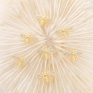 Gold bee charms with zircon crystals for DIY necklace making on coral background